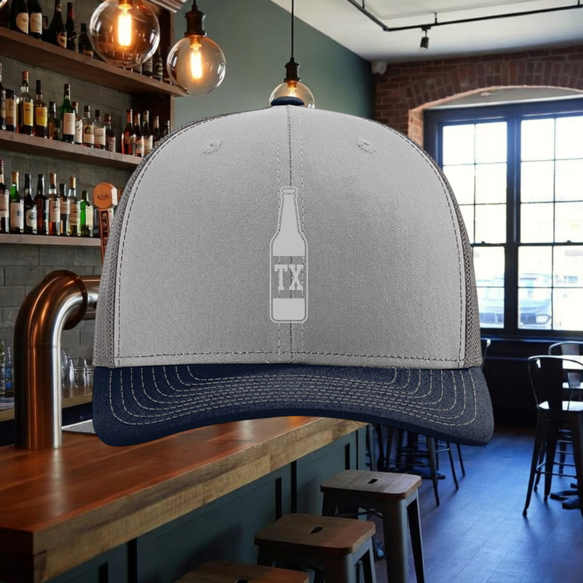 Better Grab A Beer TX Bottle trucker hat in grey and navy with a pre-curved visor and mesh back in a bar setting.